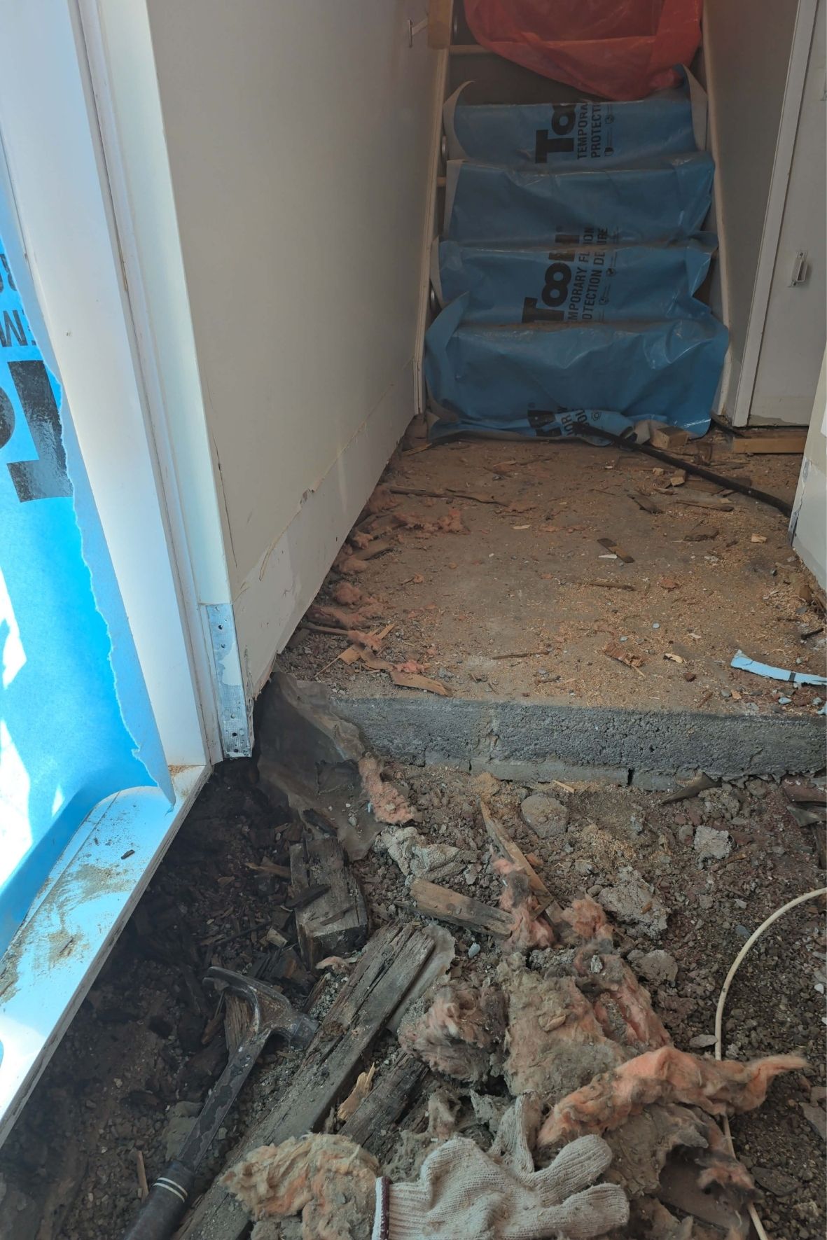 Escalier protégé par bâches plastiques et débris au sol dans un chantier intérieur  à L`Île-Bizard